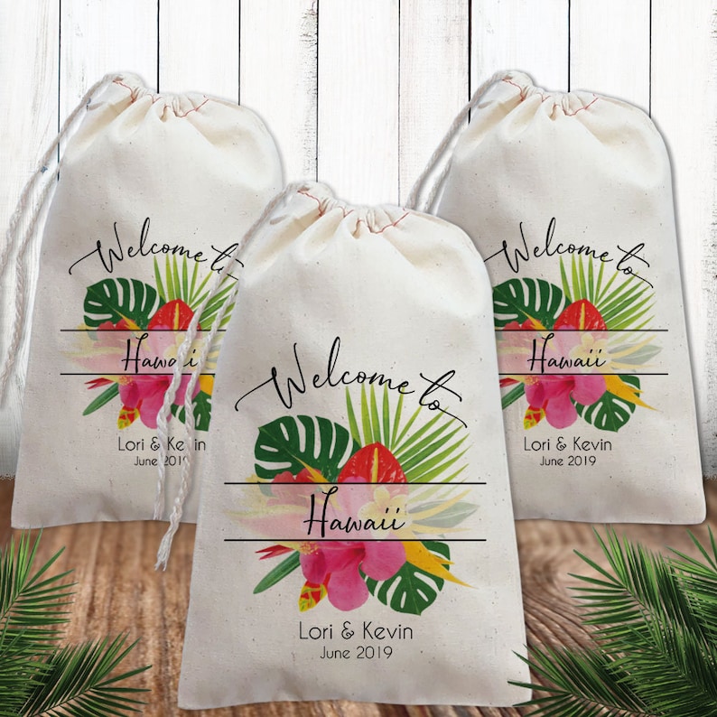 Puede incluir: Tres bolsas de algod&oacute;n blanco con cord&oacute;n de ajuste con dise&ntilde;os florales tropicales y el texto "Bienvenido a Haw&aacute;i" y "Lori & Kevin Junio 2019".