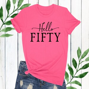 May include: Pink t-shirt with black text that says "Hello Fifty".