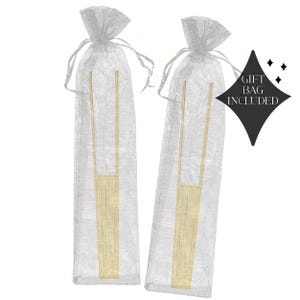May include: Two sets of gold-colored serving tongs are presented in sheer, silver gift bags. The tongs have a rectangular base and a long, slender handle. The words "GIFT BAG INCLUDED" are printed on a black diamond-shaped tag.