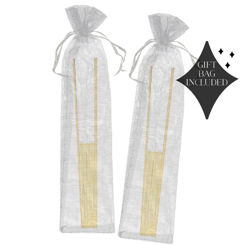 May include: Two sets of gold-colored serving tongs are presented in sheer, silver gift bags. The tongs have a rectangular base and a long, slender handle. The words "GIFT BAG INCLUDED" are printed on a black diamond-shaped tag.