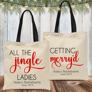 May include: Two white canvas tote bags with black handles. The bag on the left has red text that says "All the jingle ladies" and "Hailey's Bachelorette Aspen 2019". The bag on the right has red text that says "Getting merry'd" and "Hailey's Bachelorette Aspen 2019".
