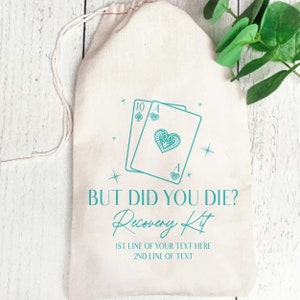 K&ouml;nnte beinhalten: Ein beigefarbener Beutel mit Kordelzug und einem t&uuml;rkisfarbenen Aufdruck von zwei Spielkarten, einer Zehn in Pik und einem Herz-Ass. Der Text lautet: BUT DID YOU DIE? Recovery Kit, gefolgt von zwei Zeilen f&uuml;r individuellen Text.