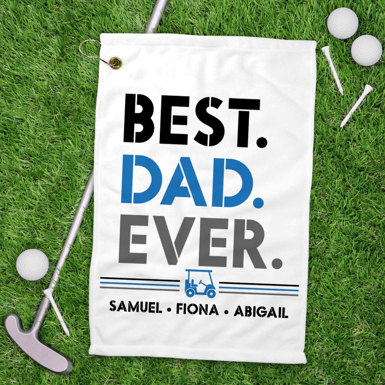 May include: White golf towel with blue and black text that reads "Best Dad Ever."  A small golf cart icon is below the text, and the names "Samuel, Fiona, Abigail" are printed below the icon.