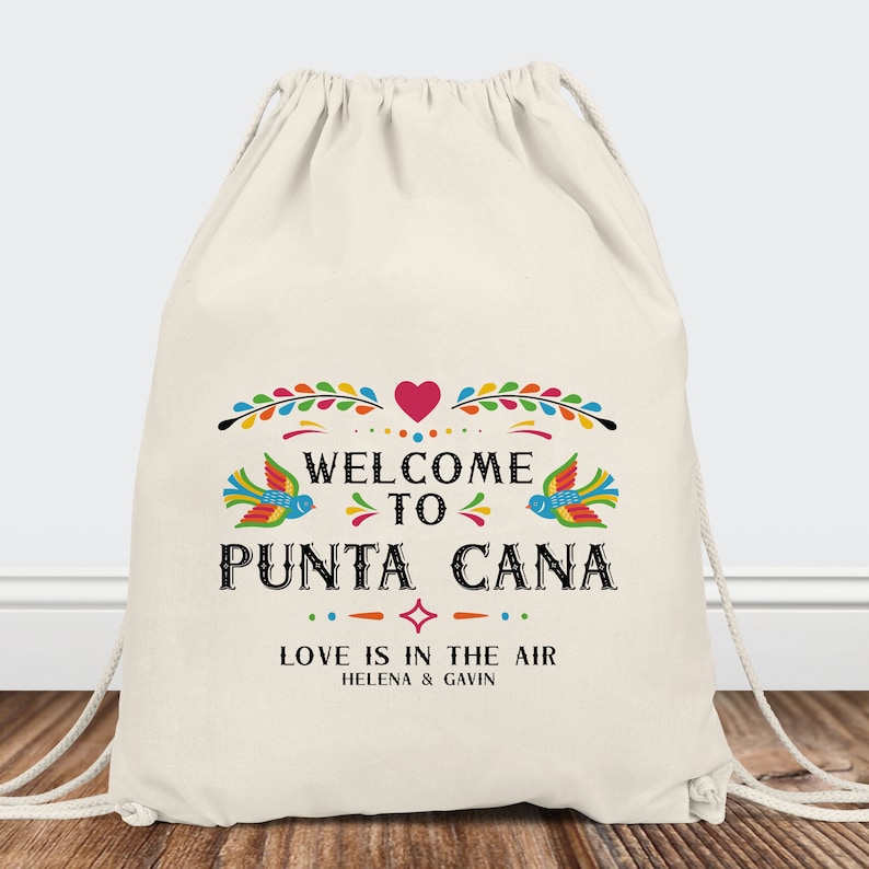 May include: A white drawstring bag with a colorful design that says "Welcome to Punta Cana" with a heart and birds. The text below says "Love is in the air" with the names Helena and Gavin.