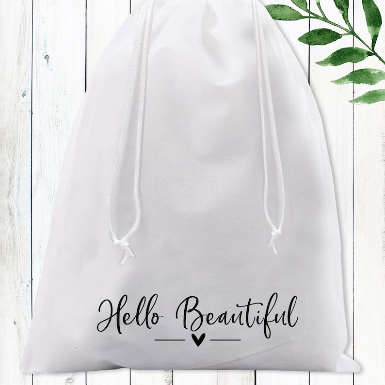 Puede incluir: Bolsa blanca de cord&oacute;n con el texto "Hello Beautiful" y un peque&ntilde;o coraz&oacute;n en letras negras.