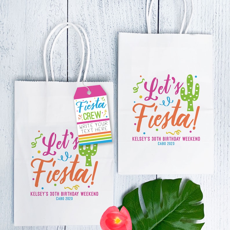 K&ouml;nnte beinhalten: Zwei wei&szlig;e Papiert&uuml;ten mit Henkeln. Die Taschen haben ein farbenfrohes Design mit dem Text "Let's Fiesta!" und "Kelsey's 30th Birthday Weekend Cabo 2023". Eine Tasche hat ein rosa Etikett mit dem Text "Fiesta Crew" und "Write your text here".