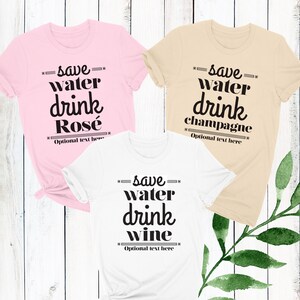 May include: Three t-shirts with the text "save water drink" and a different beverage on each shirt. The shirts are pink, beige, and white. The text is in black.