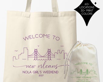 May include: A cream-colored canvas tote bag and a matching drawstring pouch. The tote features a purple skyline graphic, the text "WELCOME TO new orleans NOLA GIRL'S WEEKEND 2027," and a star-shaped graphic stating "60+ LOCATIONS 30+ PRINT COLORS."