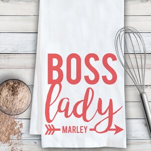 May include: White kitchen towel with the text "BOSS lady" in red cursive font with an arrow pointing to the right and the name "MARLEY" underneath.