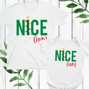 May include: Two white t-shirts with a Christmas tree design and the text "NICE (ish)". The larger shirt has a long sleeve and the smaller shirt has a short sleeve.
