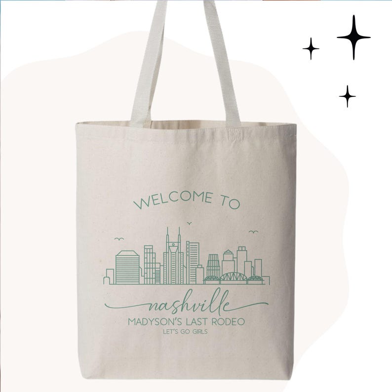 May include: Cream-colored tote bag with white handles. The bag features a green line drawing of the Nashville skyline, with the words "WELCOME TO Nashville" and "MADYSON'S LAST RODEO LET'S GO GIRLS" in green text.
