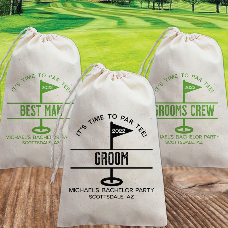 May include: Three white drawstring bags with green and black text. The bags have a golf theme and say "It's time to par tee!" with the year 2022. The bags say "Best Man", "Groom", and "Grooms Crew".