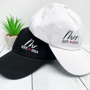 May include: Two baseball caps, one black and one white, with the words "Mr. EST. ♥ 2024" and "Mrs. EST. ♥ 2024" embroidered on them.