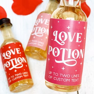 May include: Three small glass bottles filled with a golden liquid. Each bottle has a label that reads "Love Potion" in a whimsical font. The labels are in red and pink, with the option for custom text.