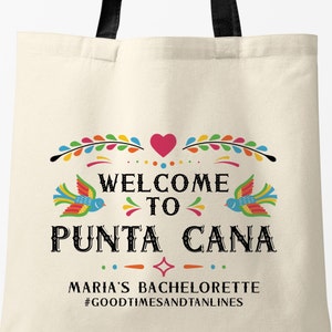 May include: A white tote bag with a colorful design that says "Welcome to Punta Cana" with a heart and birds. The text below says "Maria's Bachelorette #GoodTimesAndTanLines".