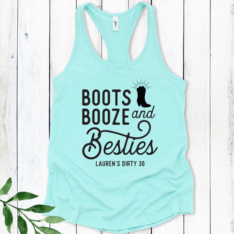 May include: A light blue tank top with black text that reads "Boots Booze and Besties" with a silhouette of a cowboy boot. The text "Lauren's Dirty 30" is printed below the main text.