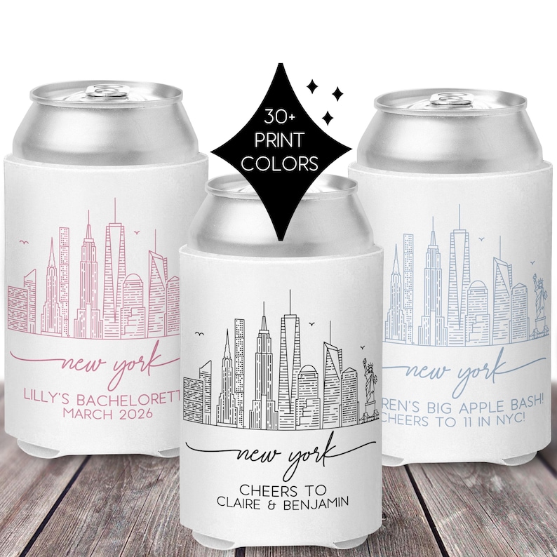 May include: Three white can coolers with New York City skyline designs. One has a pink skyline and text, another has a black skyline, and the third has a blue skyline. Text includes "New York" and event details.