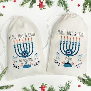 May include: Two white drawstring bags with a Hanukkah menorah design. Each bag features a blue menorah with lit candles, a Star of David, and the text "PEACE, LOVE & LIGHT". One bag says "THE HOFFMANS" and the other says "JOSHUA".
