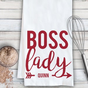 May include: White kitchen towel with red text that reads "Boss lady" with an arrow pointing to the right and the name "Quinn" underneath.