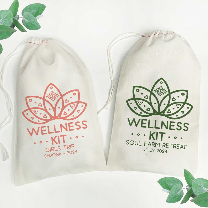 K&ouml;nnte beinhalten: Zwei cremefarbene Stoffbeutel mit Kordelzug. Der linke Beutel zeigt ein korallenfarbenes Lotus-Motiv mit dem Text WELLNESS KIT GIRLS TRIP SEDONA - 2024. Der rechte Beutel hat ein dunkelgr&uuml;nes Lotus-Motiv mit dem Text WELLNESS KIT SOUL FARM RETREAT JULY 2024.