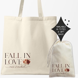 May include: Two white canvas tote bags with the text "Fall in Love" and floral designs. The larger bag has the names "erica & michael" written below the text. The smaller bag has the names "crica & michael" written below the text. The text is in a maroon color. The bags are available in totes and gift bags.