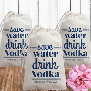 May include: Three white cotton drawstring bags with the text "save water drink vodka" printed in blue. The bags are decorated with a black border around the text. The text on the bags also includes the date "Valerie's 21st - Vegas 2022".