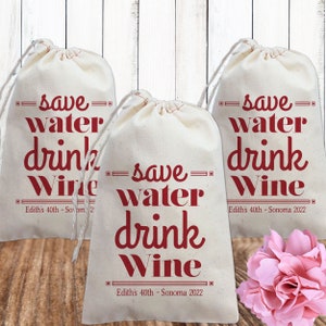 May include: Three white cotton drawstring bags with the text "save water drink wine" in red. The bags have the text "Edith's 40th - Sonoma 2022" printed on the bottom.