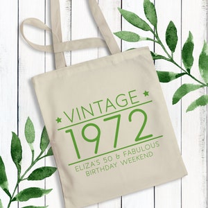 May include: A beige canvas tote bag with green text that reads "Vintage * 1972 Eliza's 50 & Fabulous Birthday Weekend".
