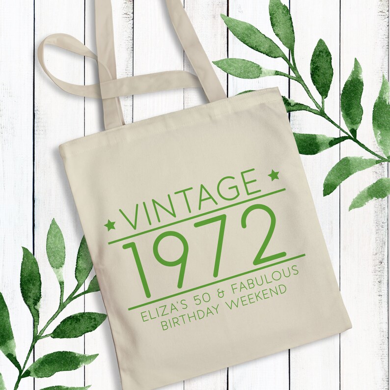 May include: A beige canvas tote bag with green text that reads "Vintage * 1972 Eliza's 50 & Fabulous Birthday Weekend".