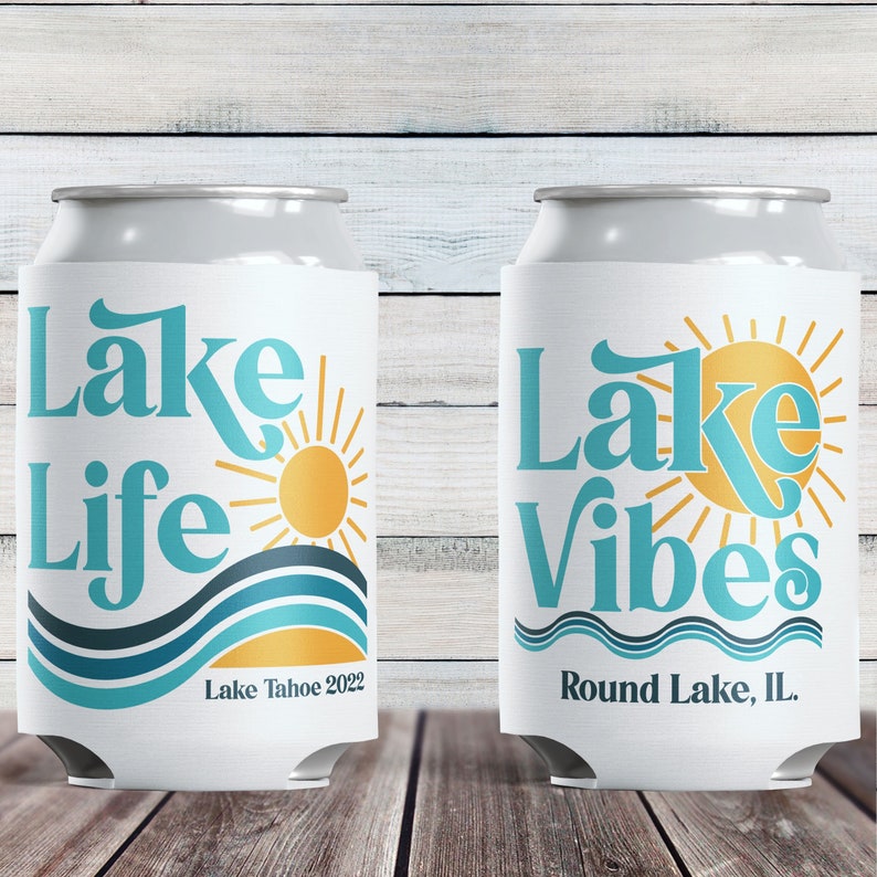 May include: Two white can coolers with blue and yellow designs. The first cooler says "Lake Life" with a sun and waves. The second cooler says "Lake Vibes" with a sun and waves. The first cooler says "Lake Tahoe 2022" and the second cooler says "Round Lake, IL."