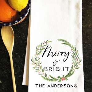May include: White kitchen towel with a green wreath design and the text "Merry & Bright The Andersons".