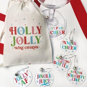 May include: A natural-colored drawstring pouch with the text HOLLY JOLLY WINE CHARMS in red, green, and blue. Six clear circular acrylic wine charms feature festive phrases including CUP OF CHEER, XMAS CHEER, HO HO HO WHOLE BOTTLE, JOLLY AF, JINGLE JUICE, and SANTA'S NAUGHTY LIST.