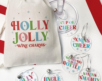 May include: A natural-colored drawstring pouch with the text HOLLY JOLLY WINE CHARMS in red, green, and blue. Six clear circular acrylic wine charms feature festive phrases including CUP OF CHEER, XMAS CHEER, HO HO HO WHOLE BOTTLE, JOLLY AF, JINGLE JUICE, and SANTA'S NAUGHTY LIST.