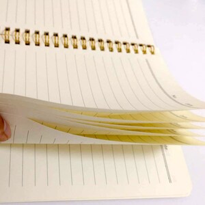 May include: A spiral bound notebook with lined pages. The pages are fanned out to show the cream colored paper.