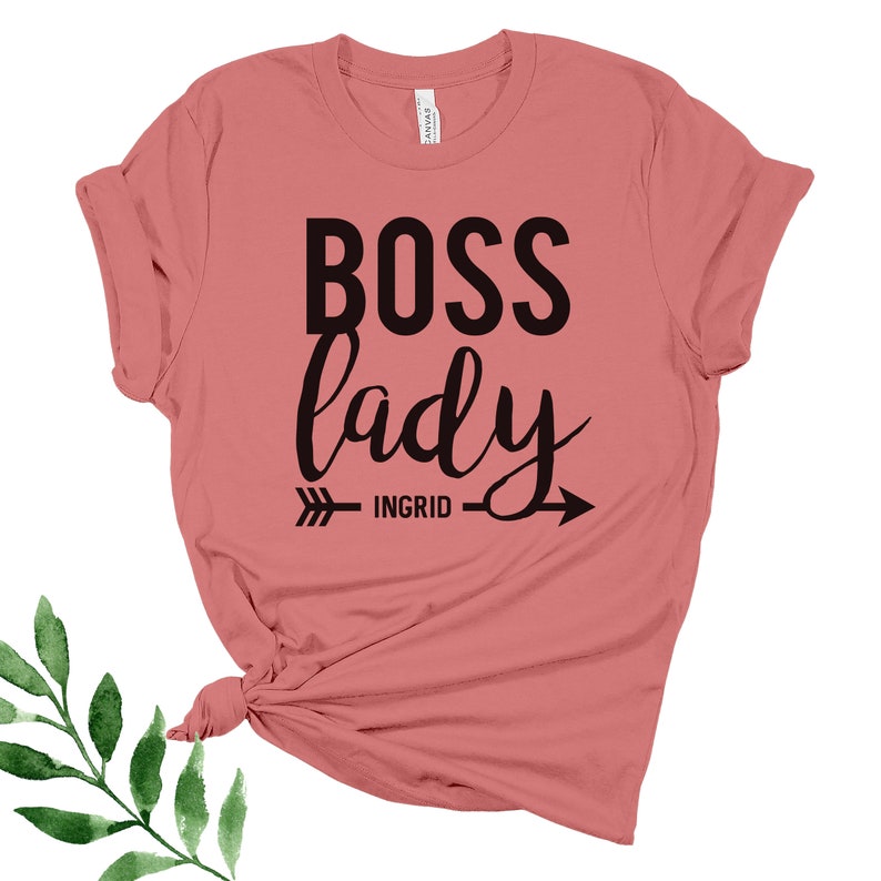 May include: A pink t-shirt with the text "BOSS lady" in black lettering. An arrow with the text "INGRID" is below the text.
