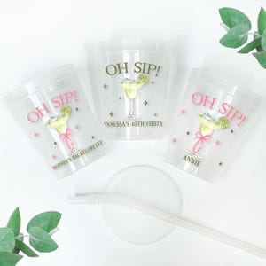 Op de afbeelding: Drie doorzichtige plastic bekers met de tekst OH SIP! in roze of goud, vergezeld van een illustratie van een margaritaglas met een schijfje limoen en een roze strik. Elke beker is gepersonaliseerd met namen zoals Sophia, Vanessa of Annie.