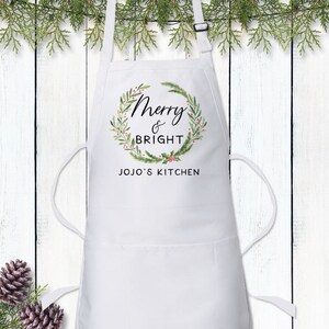 May include: White kitchen apron with a green and red wreath design and the text "Merry & Bright" and "JOJO'S KITCHEN".