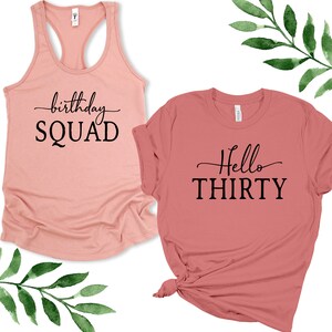 May include: Two pink t-shirts with black text. One shirt says "birthday SQUAD" and the other says "Hello THIRTY".