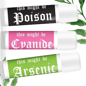 Könnte beinhalten: Drei zylindrische Lippenbalsamstifte mit weißen Kappen. Der obere Stift ist schwarz mit weißem Text this might be Poison. Der mittlere Stift ist rosa mit weißem Text this might be Cyanide. Der untere Stift ist grün mit weißem Text this might be Arsenic.