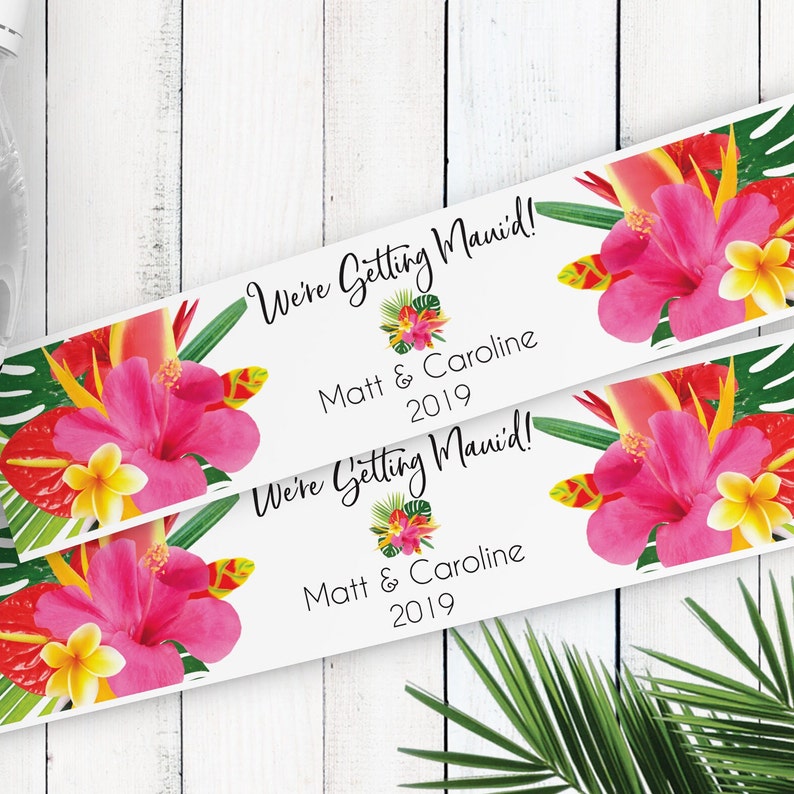 Puede incluir: Dos etiquetas blancas con dise&ntilde;os florales tropicales y el texto "We're Getting Maui'd!" con los nombres Matt & Caroline y el a&ntilde;o 2019.