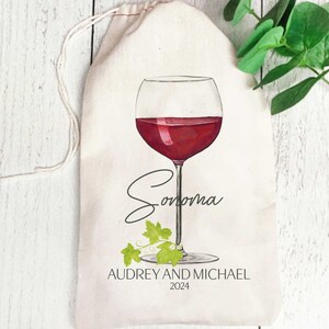 May include: A white canvas wine bag with a red wine glass illustration and the text "Sonoma" in cursive. The bag also includes the text "Audrey and Michael 2024".