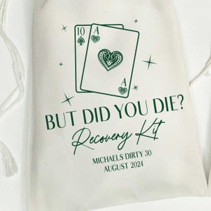 K&ouml;nnte beinhalten: Ein cremefarbener Beutel mit Kordelzug und einem dunkelgr&uuml;nen Aufdruck von einer Zehn in Pik und einem Herz-Ass. Der Text lautet BUT DID YOU DIE? Recovery Kit, MICHAELS DIRTY 30 und AUGUST 2024, umgeben von kleinen Sternsymbolen.