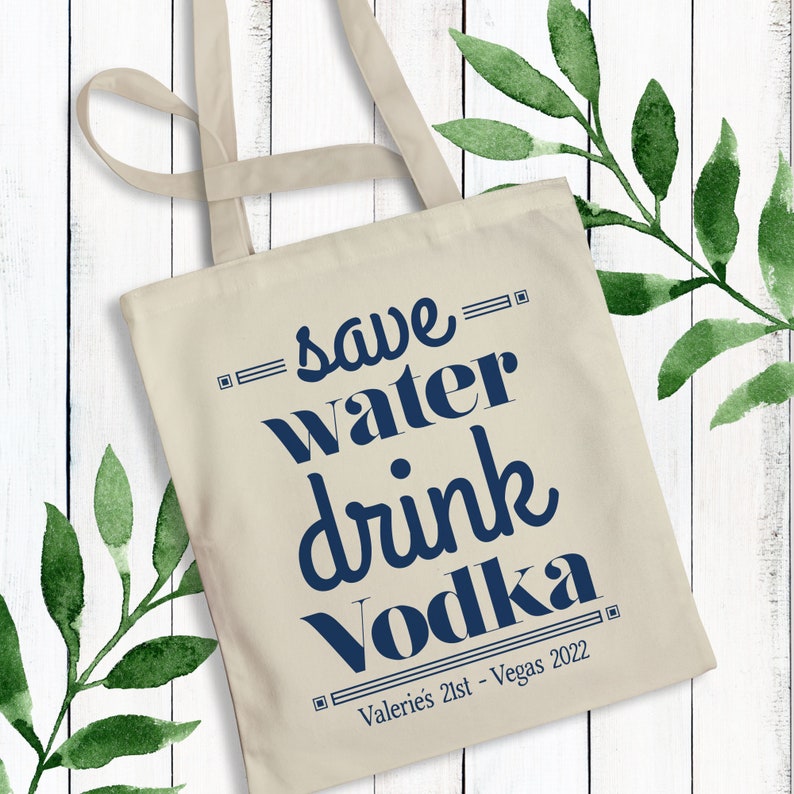 May include: A white canvas tote bag with blue text that reads "Save water drink vodka" and "Valeries 21st - Vegas 2022".