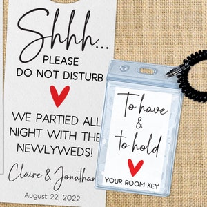 May include: A white card with the text "Shhh... Please Do Not Disturb" and a red heart. Below the text is "We partied all night with the newlyweds!" and the names "Claire & Jonathan" and the date "August 22, 2022". A clear plastic card holder with a black lanyard attached to it has the text "To have & to hold" and a red heart. Below the text is "Your Room Key".