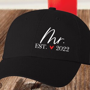 May include: Black baseball cap with white embroidery that reads "Mr. EST. &hearts; 2022".