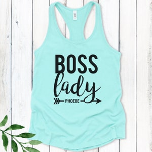 May include: A turquoise tank top with the text "BOSS lady" in black lettering and an arrow with the word "PHOEBE" underneath.