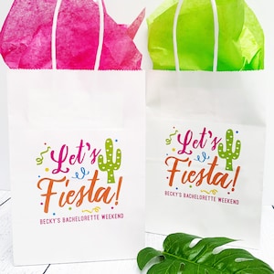 K&ouml;nnte beinhalten: Zwei wei&szlig;e Papiert&uuml;ten mit Henkeln. Die Taschen haben ein farbenfrohes Design mit dem Text "Let's Fiesta!" und einer Kaktusgrafik. Der Text "Becky's Bachelorette Weekend" ist unter dem Design gedruckt.
