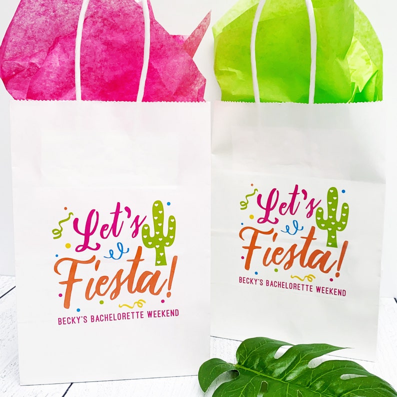 K&ouml;nnte beinhalten: Zwei wei&szlig;e Papiert&uuml;ten mit Henkeln. Die Taschen haben ein farbenfrohes Design mit dem Text "Let's Fiesta!" und einer Kaktusgrafik. Der Text "Becky's Bachelorette Weekend" ist unter dem Design gedruckt.
