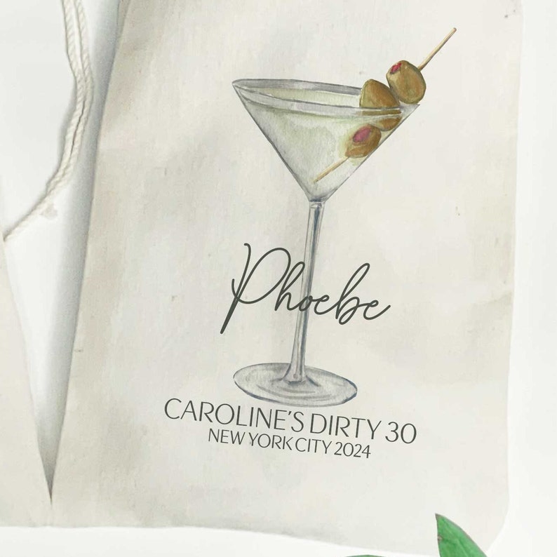Może przedstawiać: Biała karta z ilustracją kieliszka do martini i zielonych oliwek. Tekst "Phoebe" jest napisany kursywą pod kieliszkiem. Tekst "CAROLINE'S DIRTY 30 NEW YORK CITY 2024" jest wydrukowany pod nazwą.