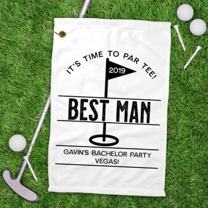 May include: White golf towel with black text: "IT'S TIME TO PAR TEE!" above a flag with "2019" and "BEST MAN" below. The text "GAVIN'S BACHELOR PARTY VEGAS!" is at the bottom. Golf balls, tees, and a putter are on the green grass.